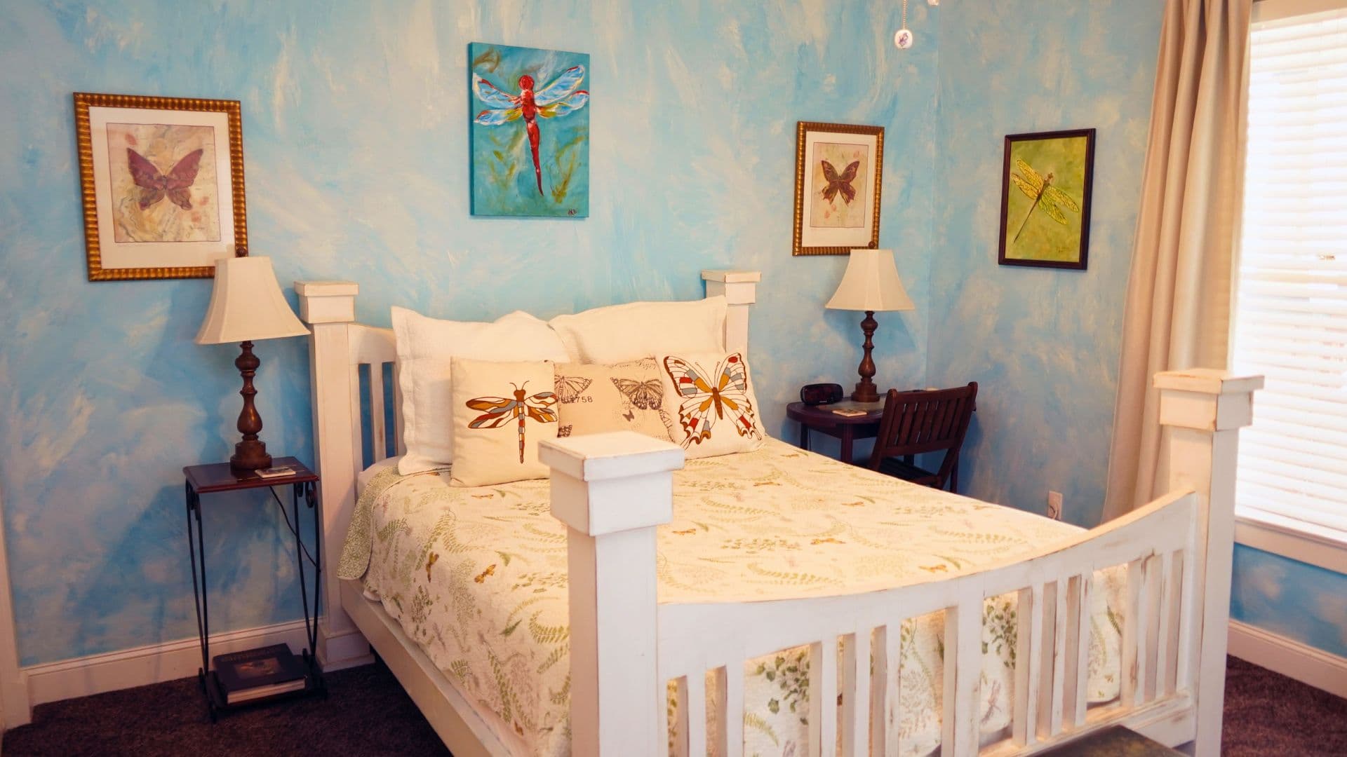 A cozy bedroom with a white bed, decorative pillows, and butterfly-themed artwork on light blue walls.