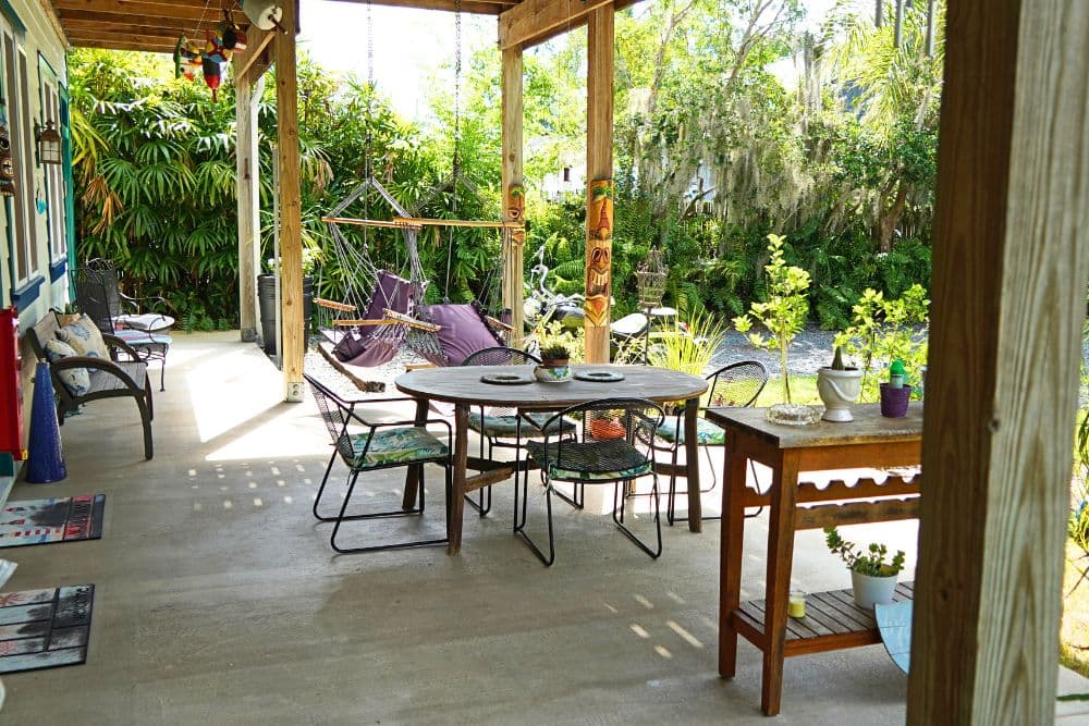 A cozy outdoor patio with a dining table, lounge chairs, and a hammock surrounded by lush greenery.