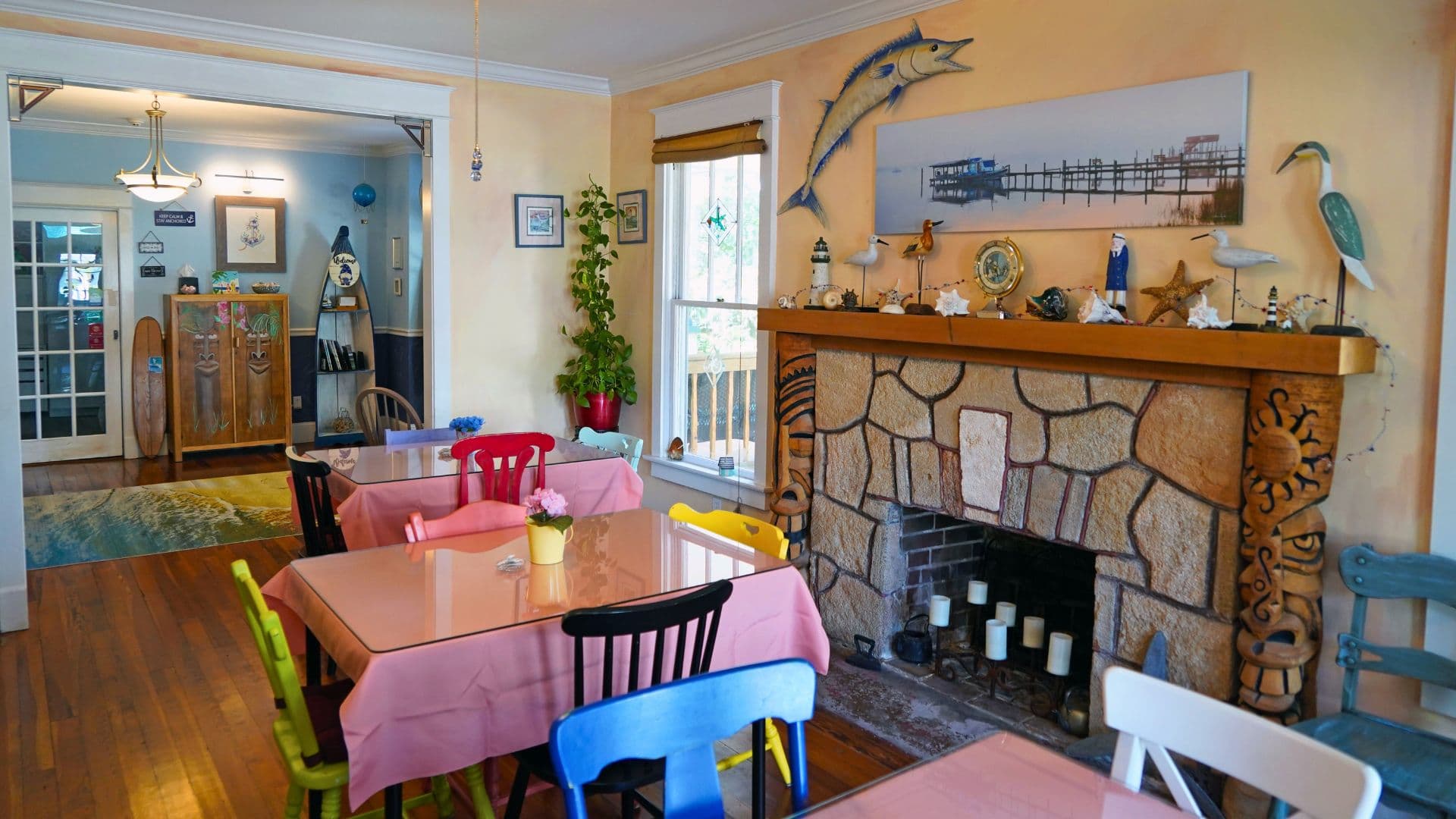 A cozy dining area featuring colorful chairs, a stone fireplace, and beach-themed decor.