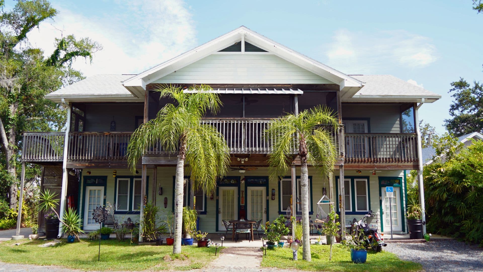 Two-story house with a porch, surrounded by greenery and decorative plants.