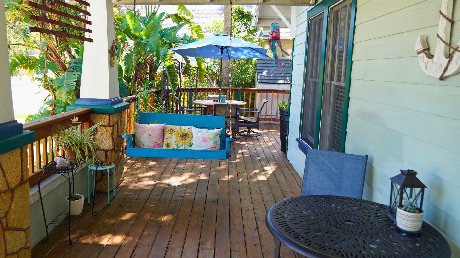 A vibrant porch featuring a blue swing, table with chairs, and lush greenery.
